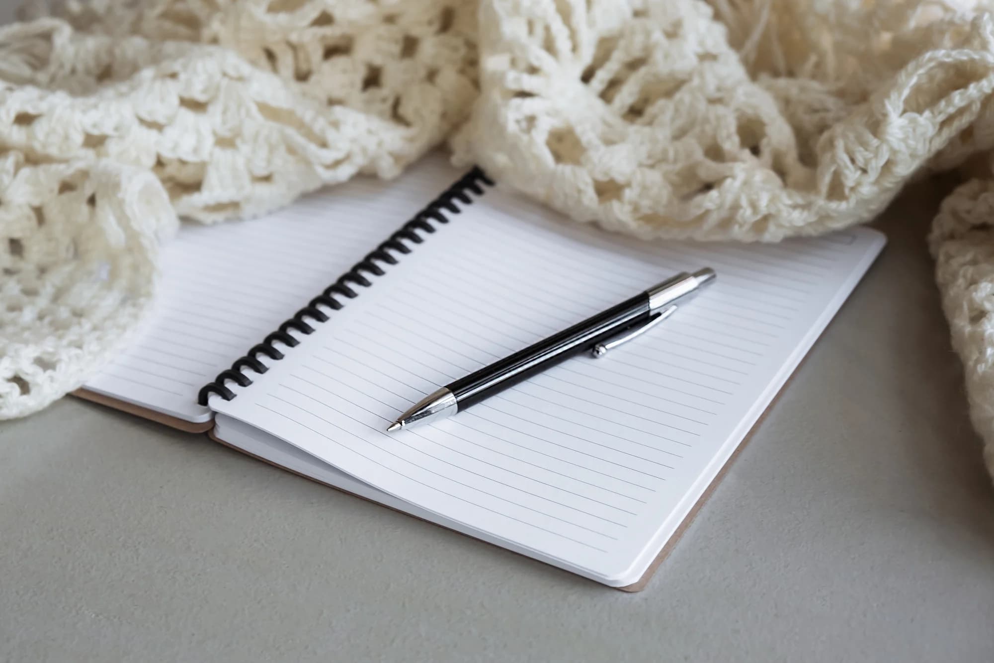 An open lined notebook and pen beside a cream knitted textile